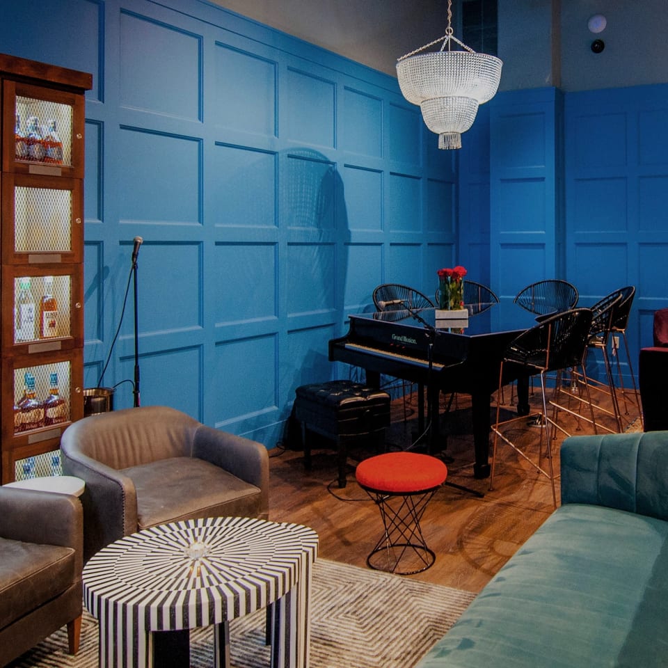 A vibrant blue lounge area with a piano, various seating, and a liquor cabinet.
