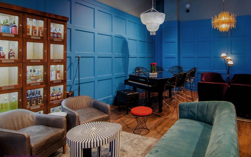 A vibrant blue lounge area with a piano, various seating, and a liquor cabinet.