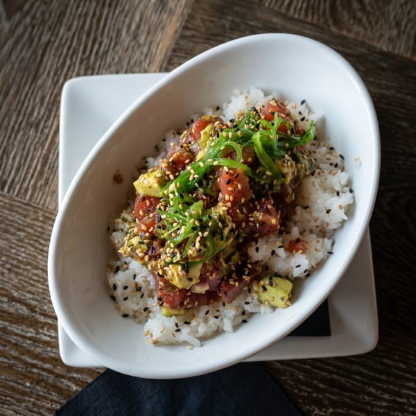 A white bowl filled with rice, tuna poke, avocado, seaweed, and sesame seeds.