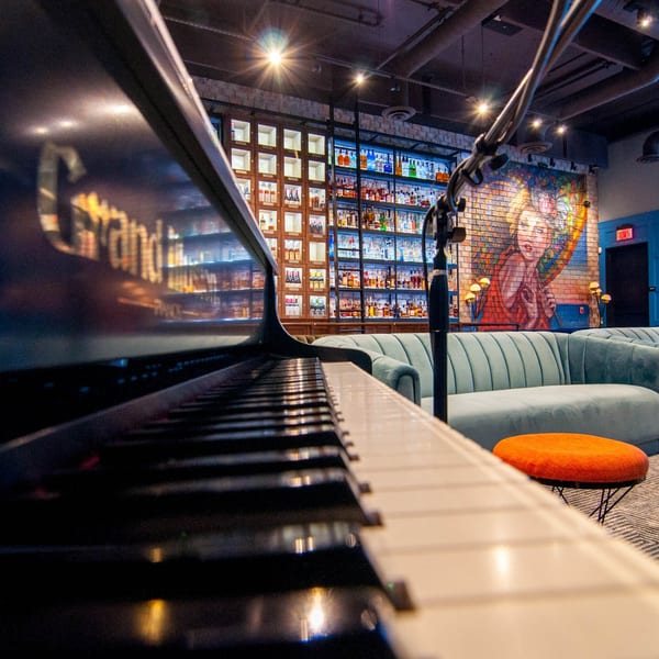 Grand piano in a lounge with a bar, light blue couches, and a colorful mural.