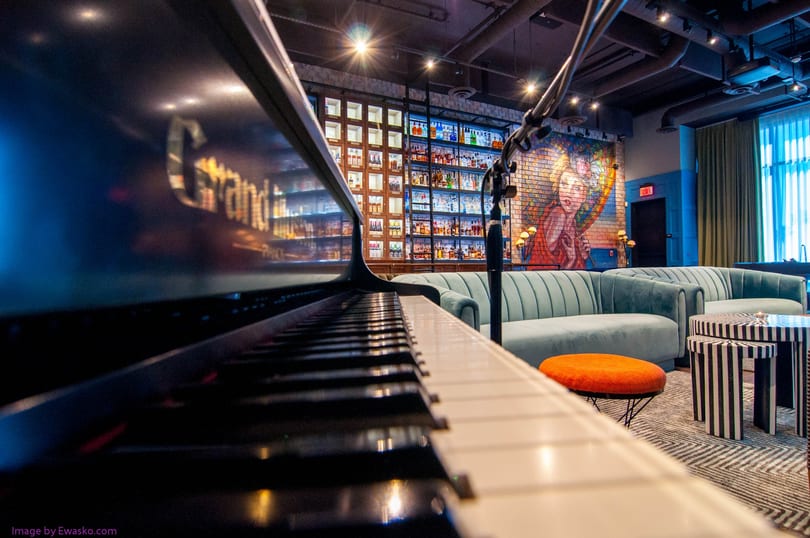 Grand piano in a lounge with a bar, light blue couches, and a colorful mural.