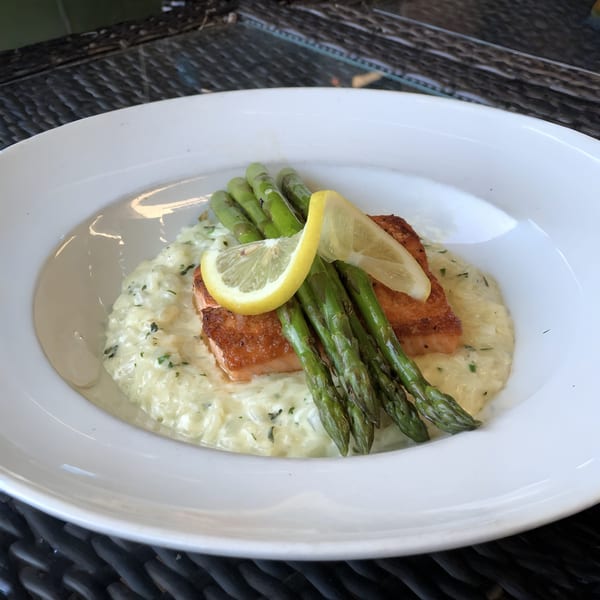 Pan-seared salmon with asparagus and creamy risotto, garnished with lemon slices, on a white plate.