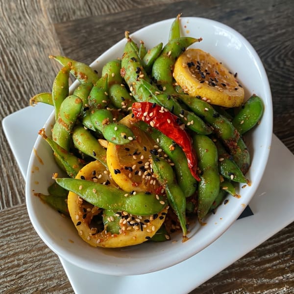 Spicy edamame with lemon slices, red chili, and sesame seeds in a white bowl.